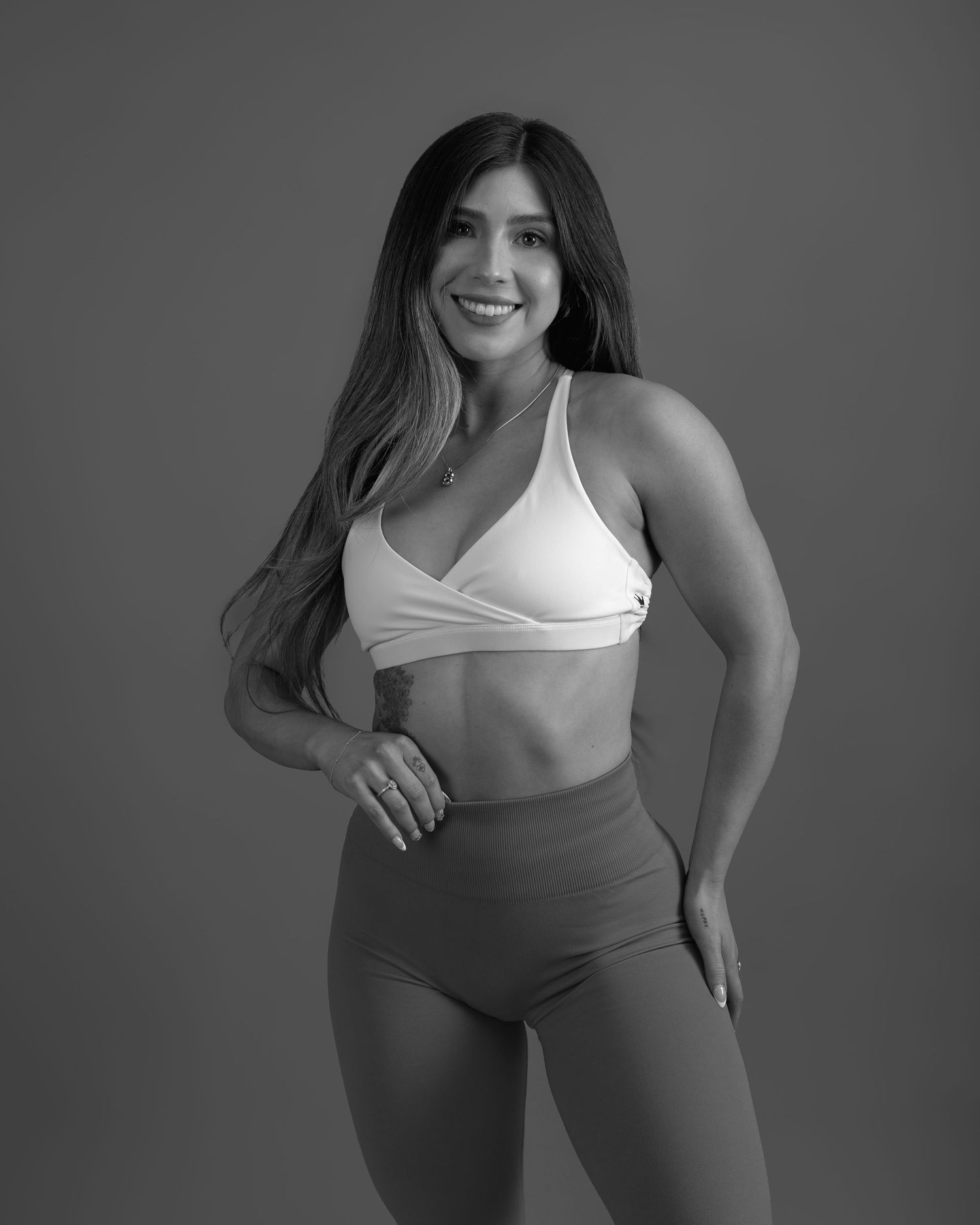 Black and white photo of a smiling woman in a white sports bra and high-waist leggings posing.