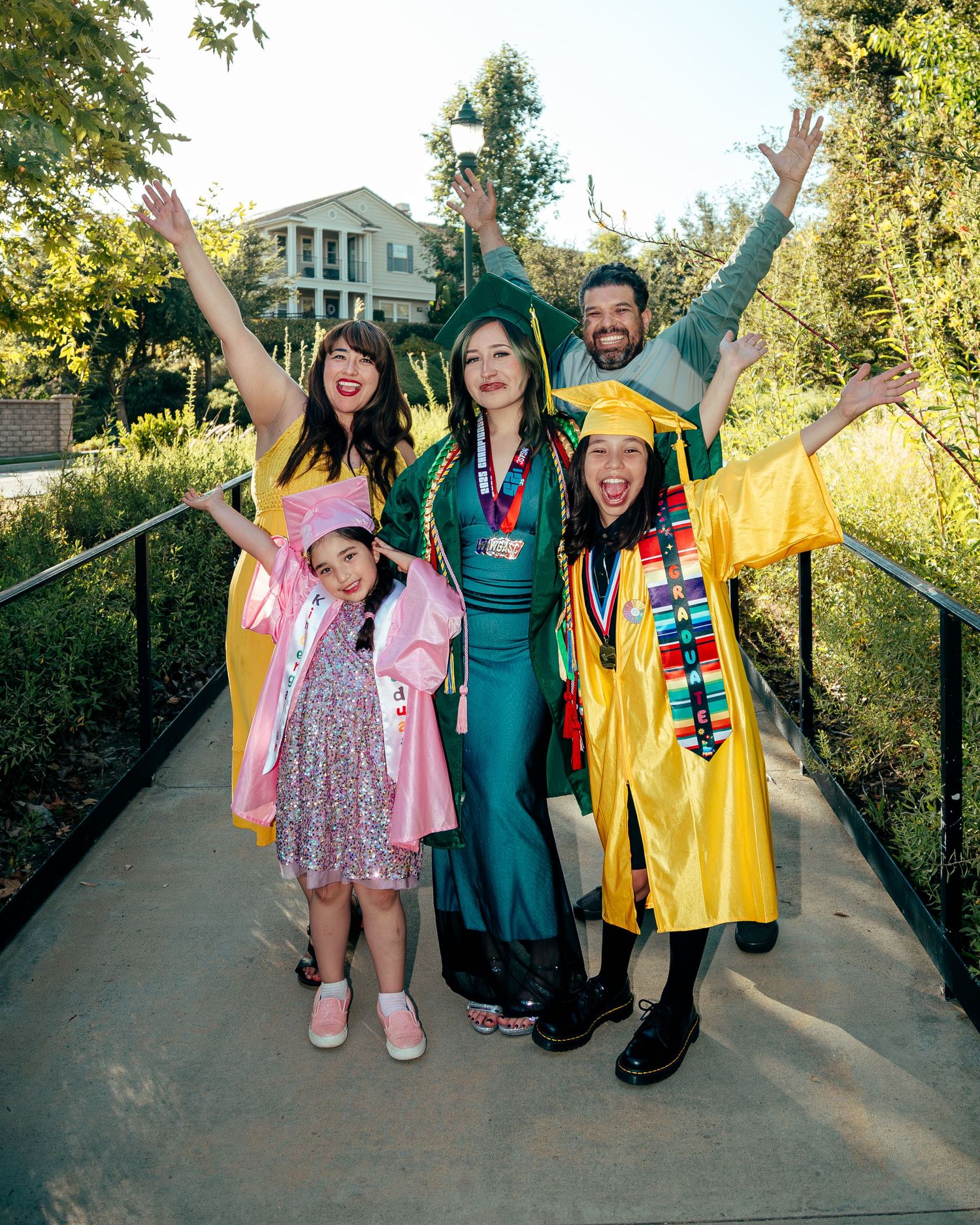 Joyful group of five celebrating graduation in colorful caps and gowns on an outdoor bridge.