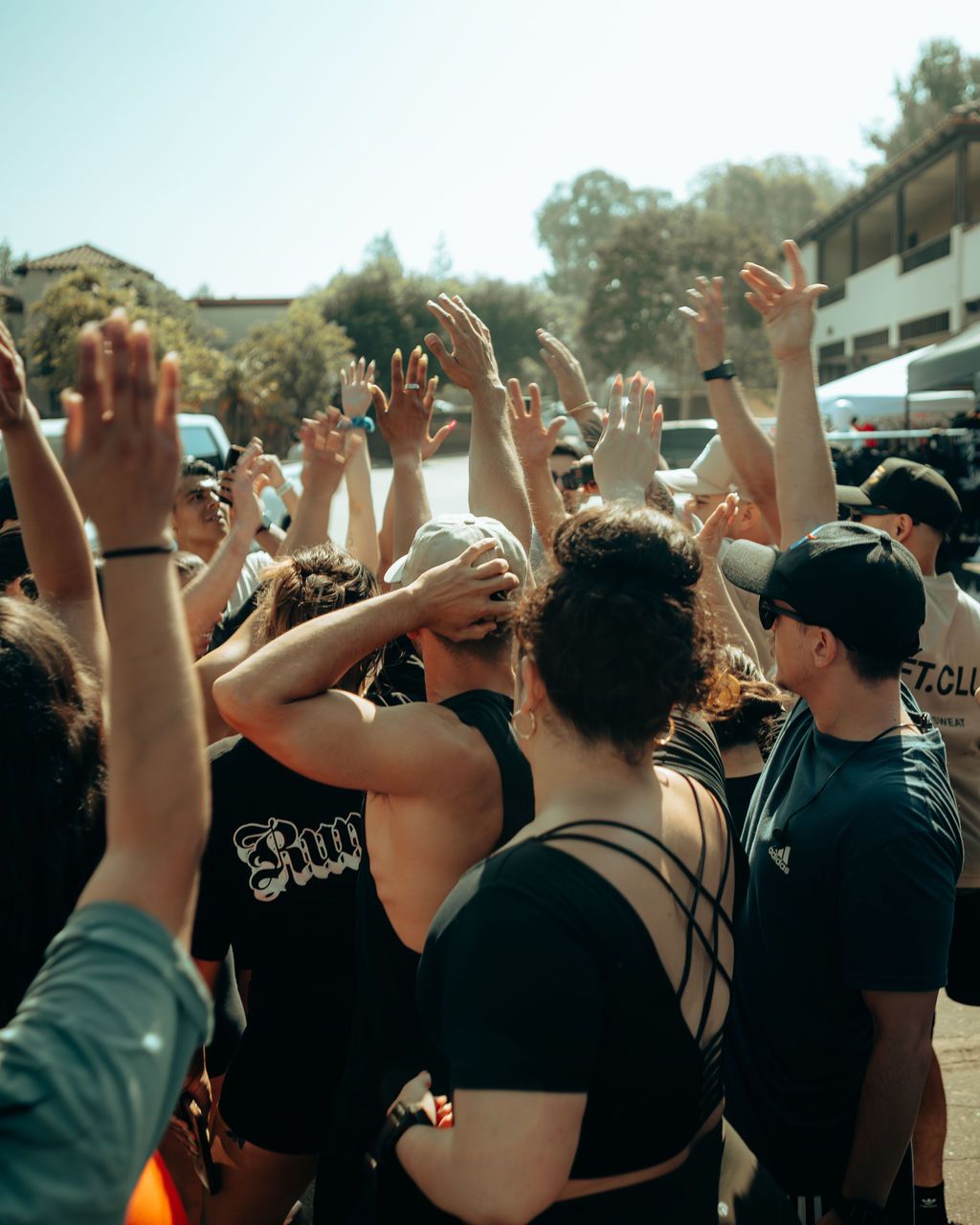 Group of people raise hands together in a sunny outdoor team huddle or celebration.