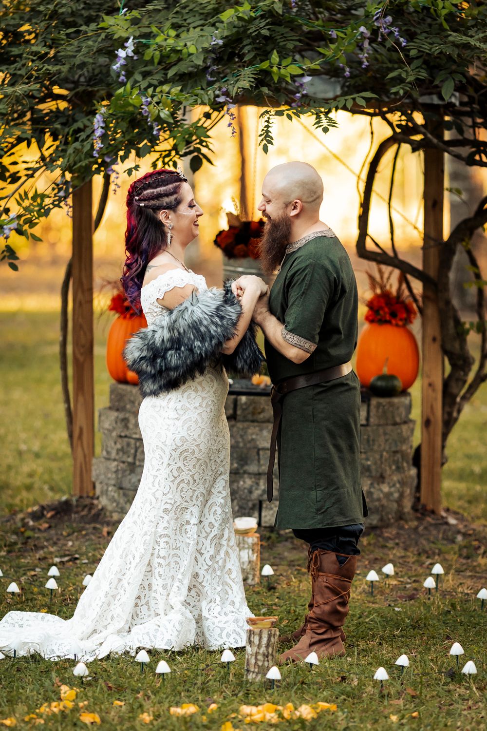 Bride in lace gown and groom in green Viking tunic share joyful moment at outdoor wedding.