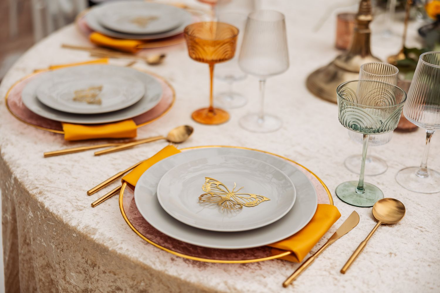 Wedding place setting with gray plates, gold butterfly detail, yellow napkin, and amber glasses.