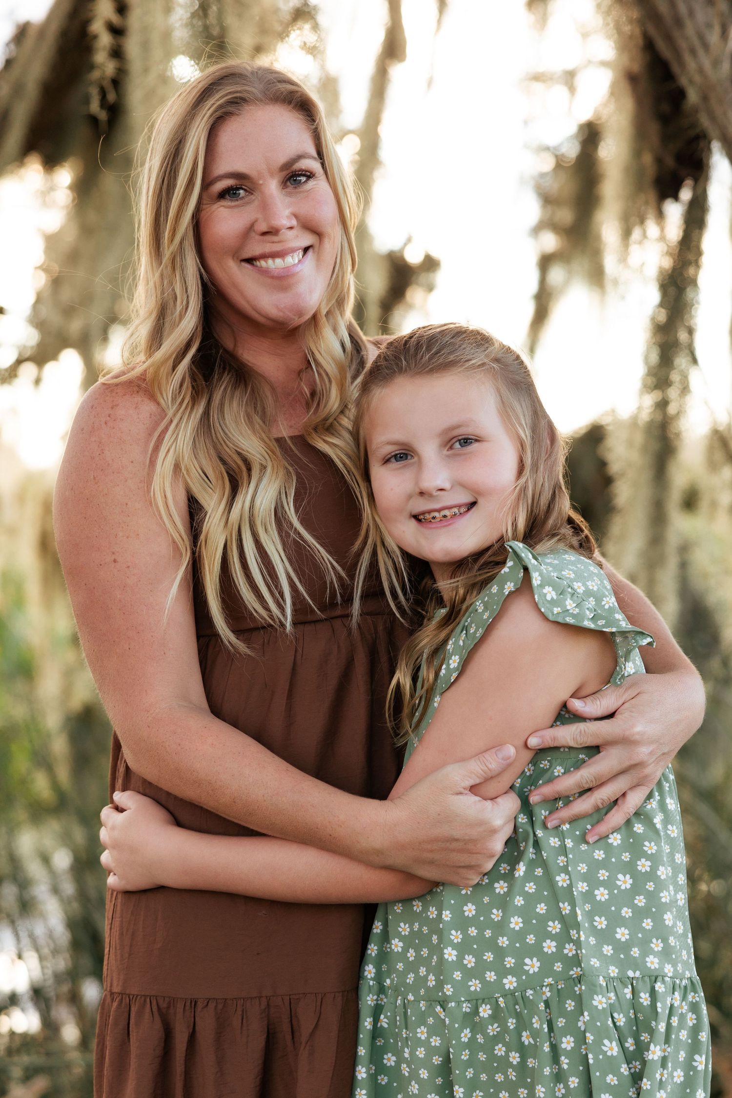 Mother and daughter embrace while wearing coordinating dresses outdoors.