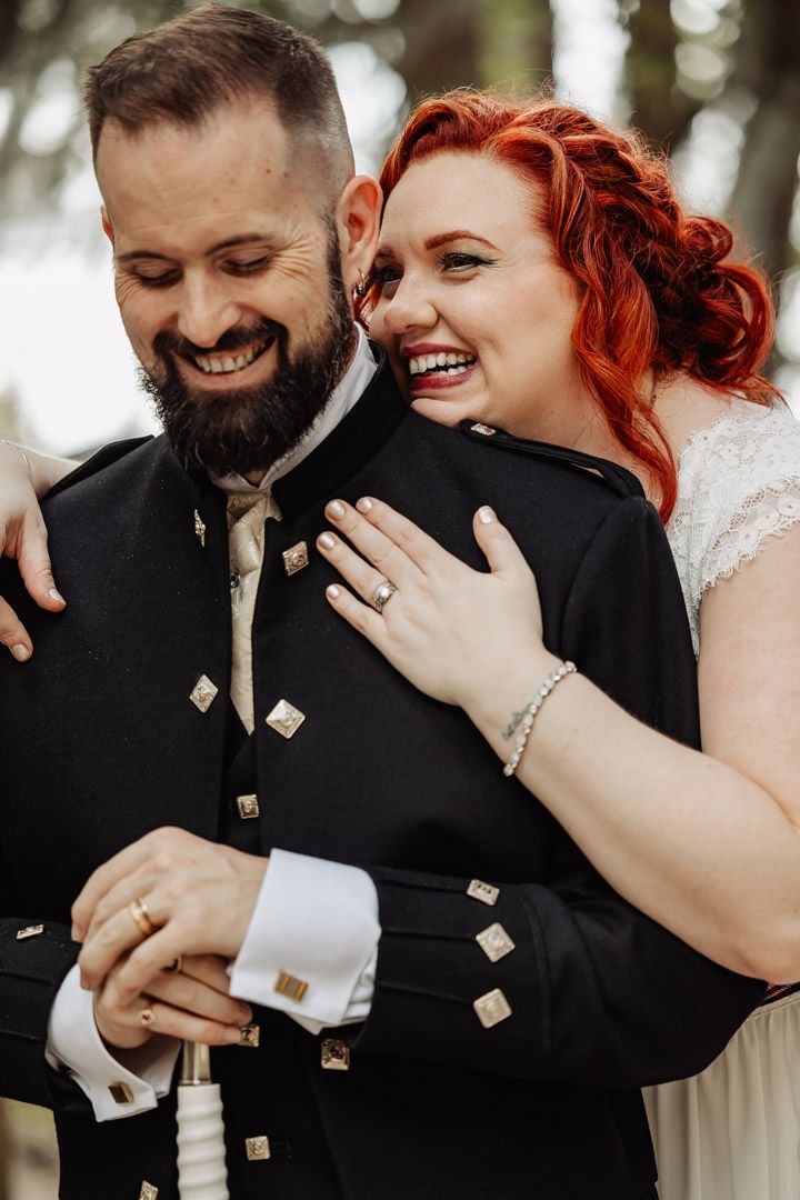 Candid moment of laughter between newlyweds in Scottish wedding attire.
