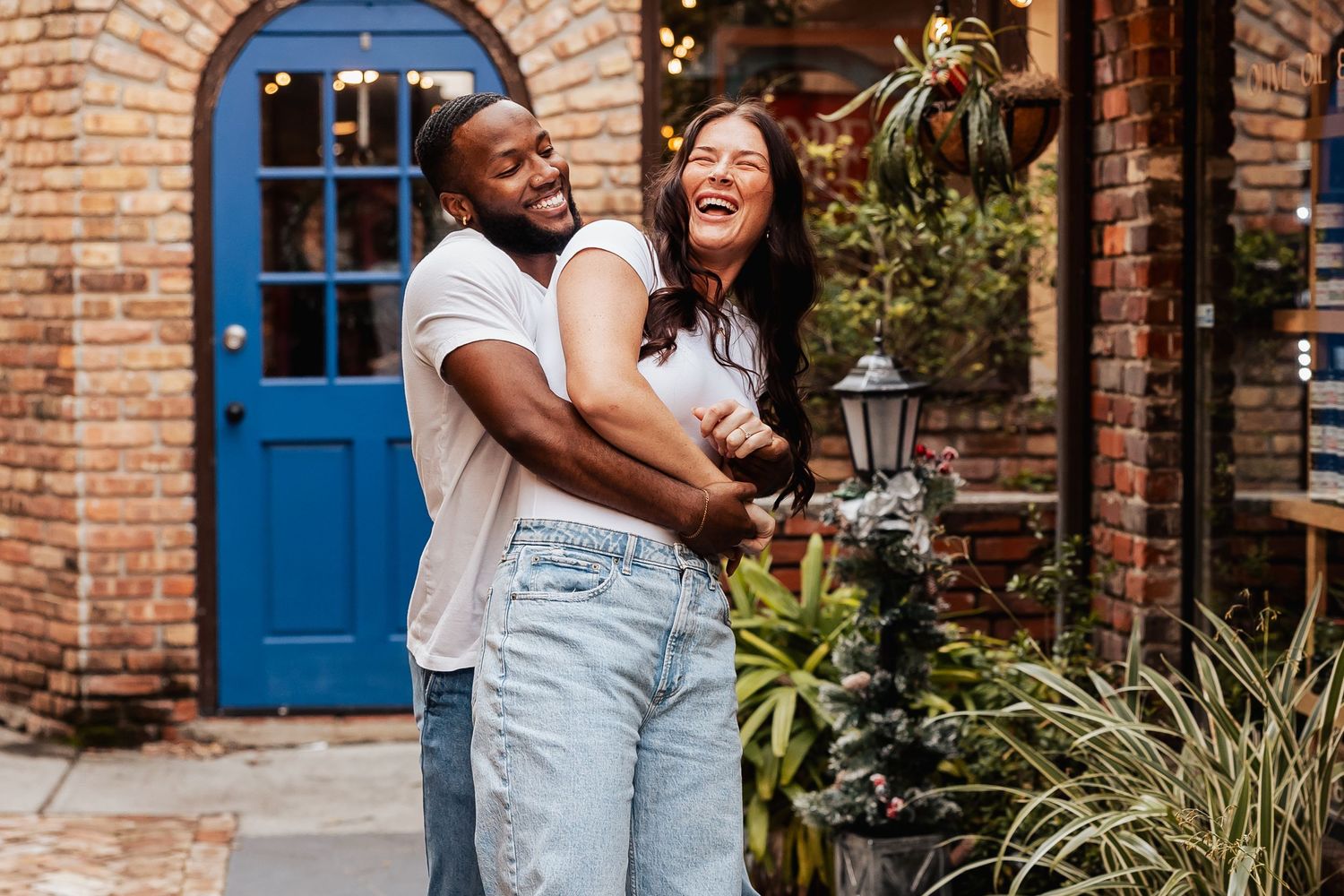 Joyful couple laughing together in front of brick building with blue door.