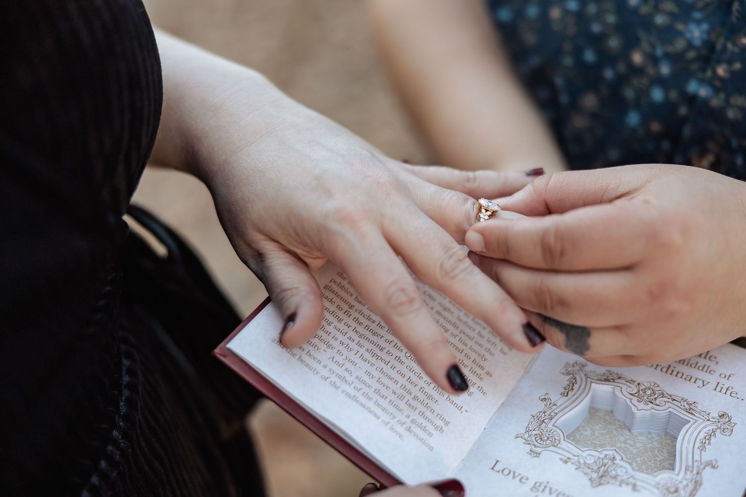 Close-up of ring exchange during outdoor wedding ceremony over an open book.