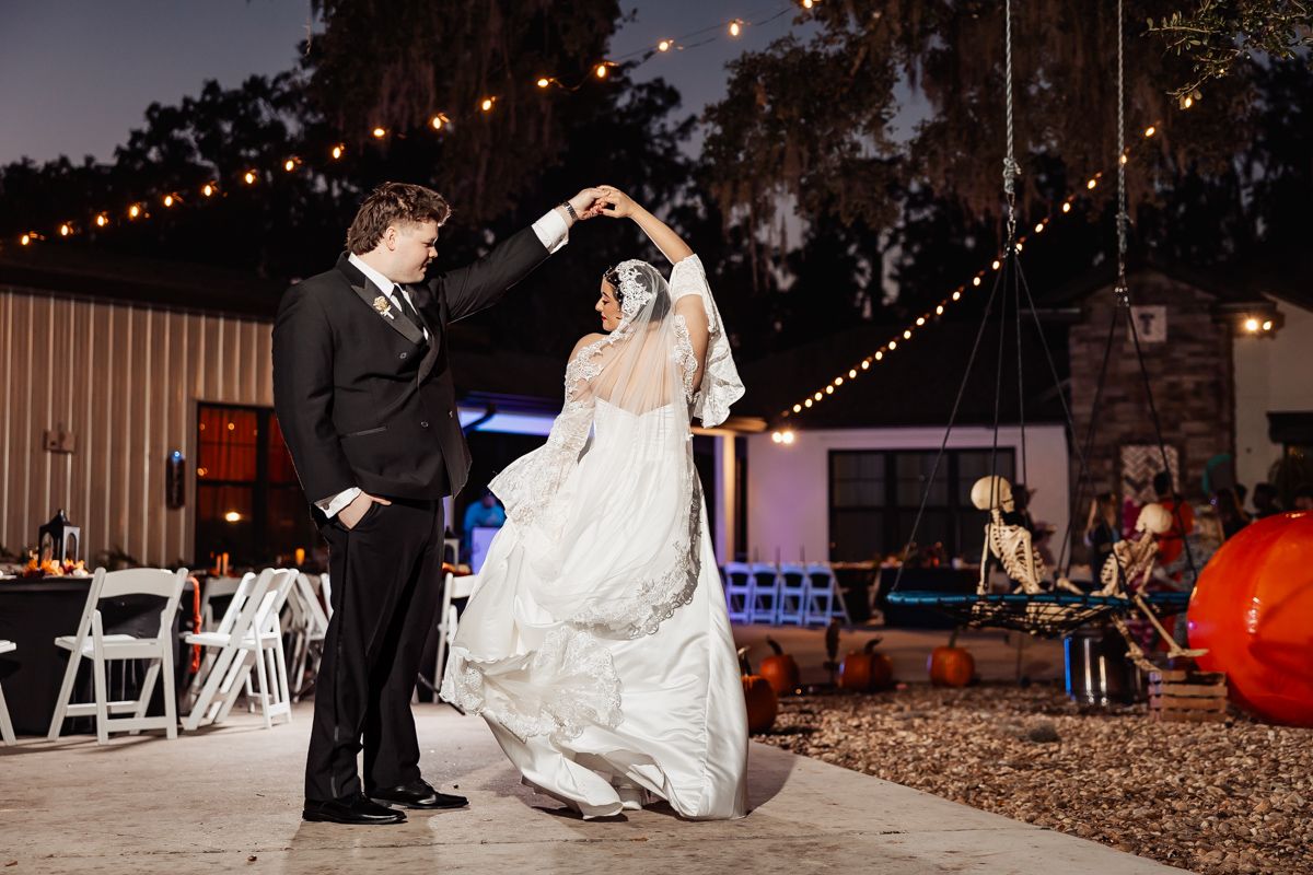 Bride and groom share first dance at outdoor Halloween wedding with string lights and skeleton decor.