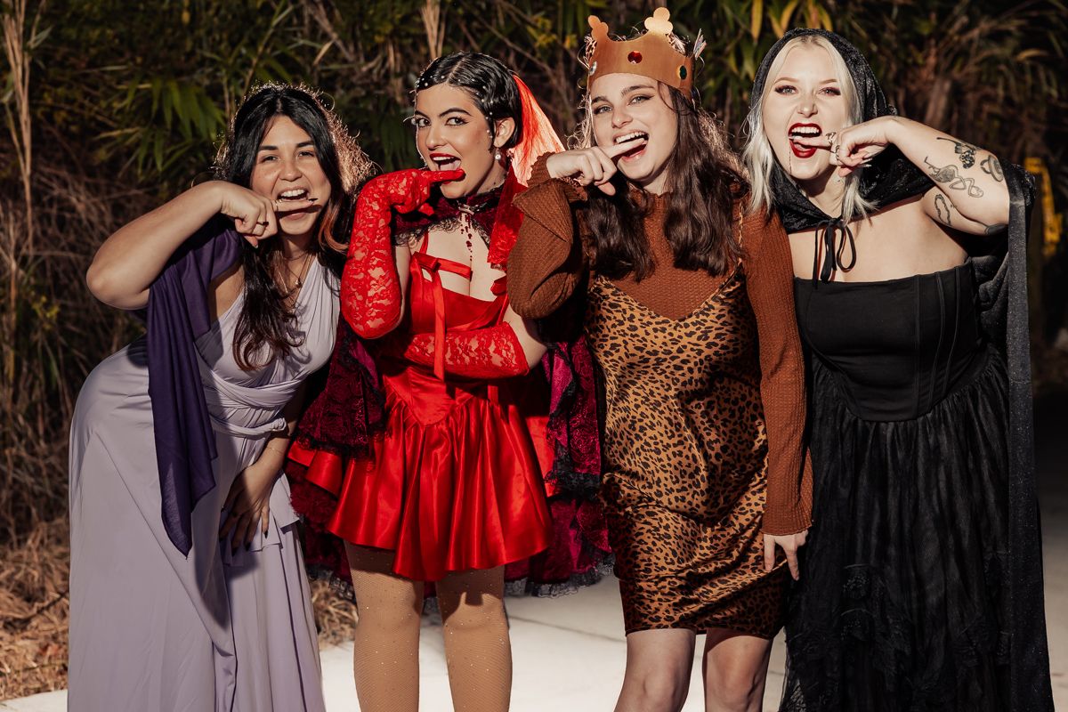Group of friends dancing and laughing together at a party wearing colorful dresses and festive outfits.
