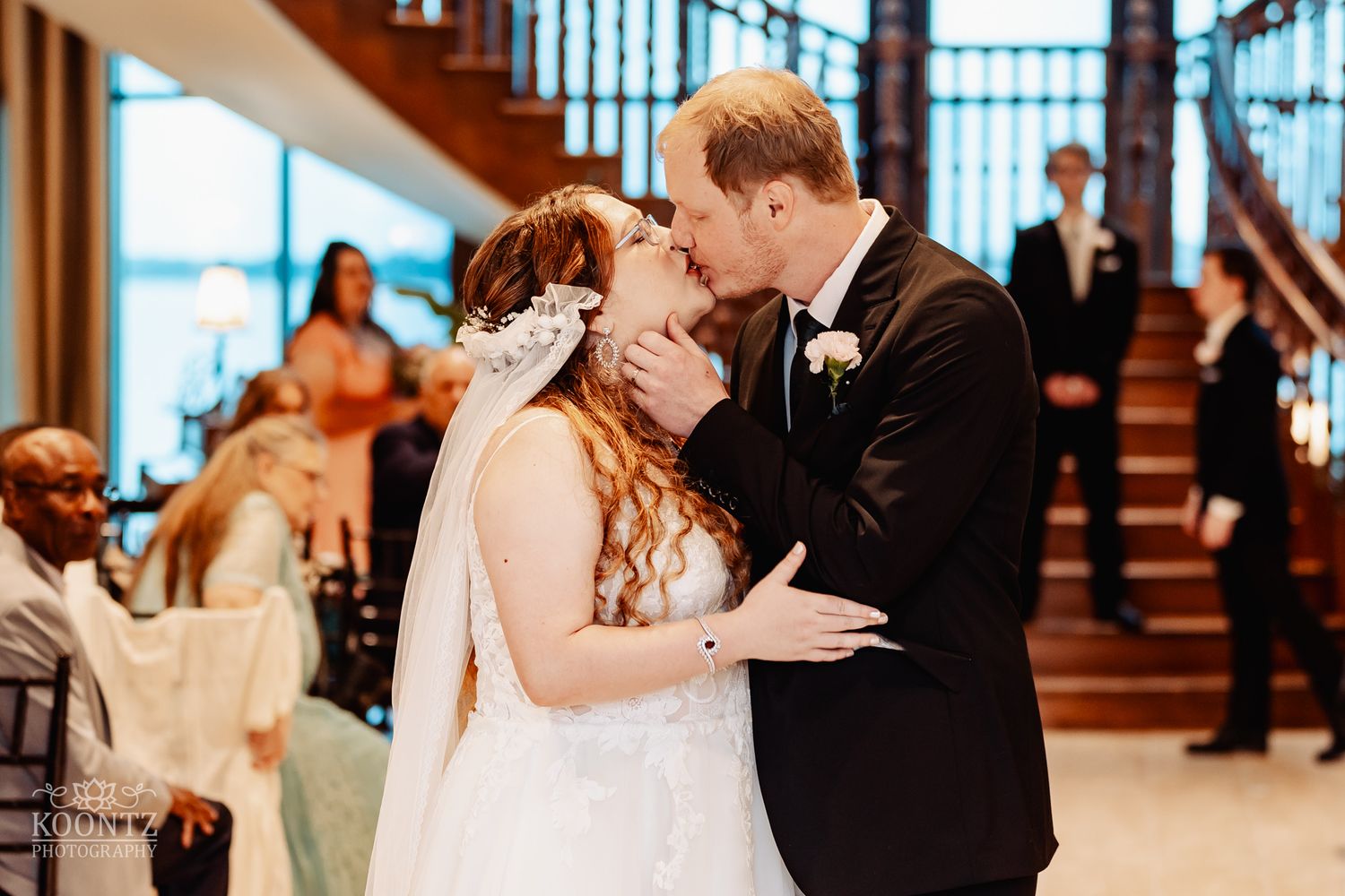 Romantic kiss during wedding reception with guests watching in background.