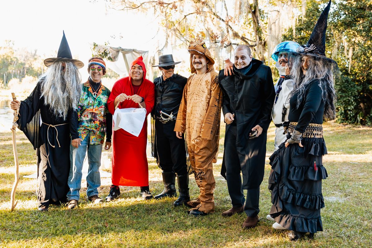 A group in Halloween costumes including a wizard, red riding hood, animal onesie and witches pose together outdoors.