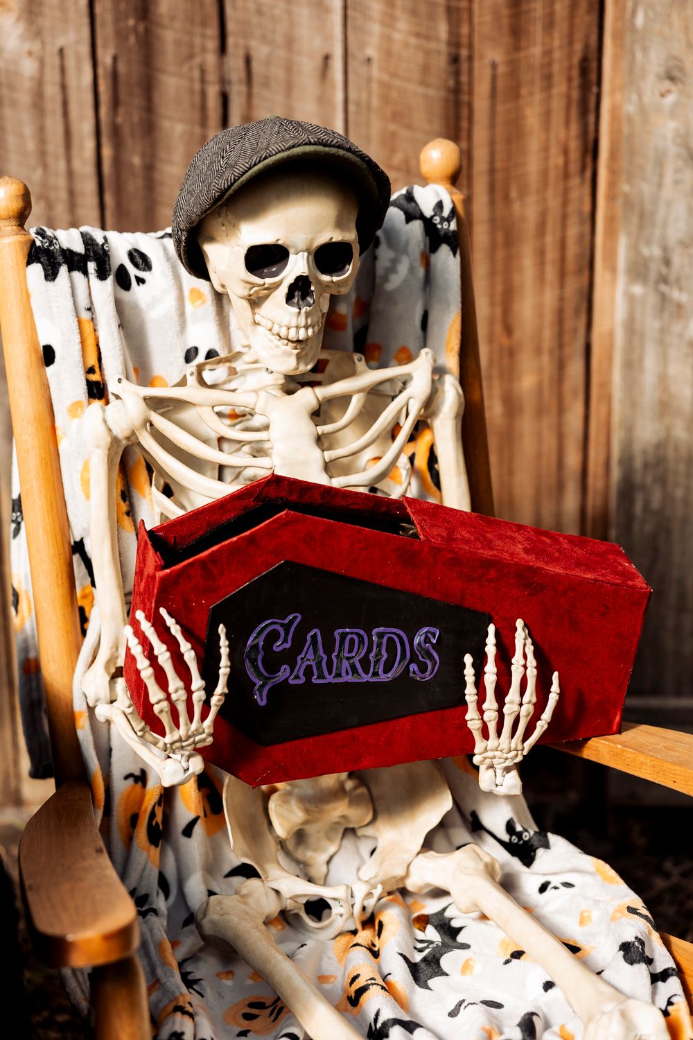 Skeleton decoration wearing newsboy cap holding red velvet card box.