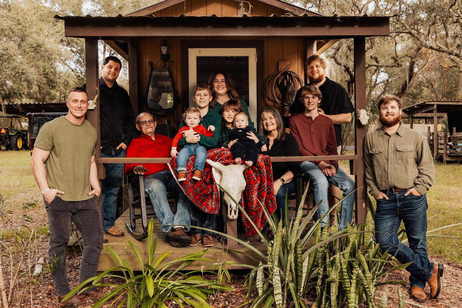 Large extended family group portrait on a wooden porch surrounded by trees and natural landscaping.