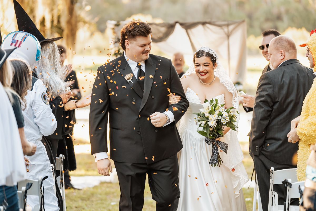 Joyful bride and groom walk down the aisle as guests shower them with colorful confetti.