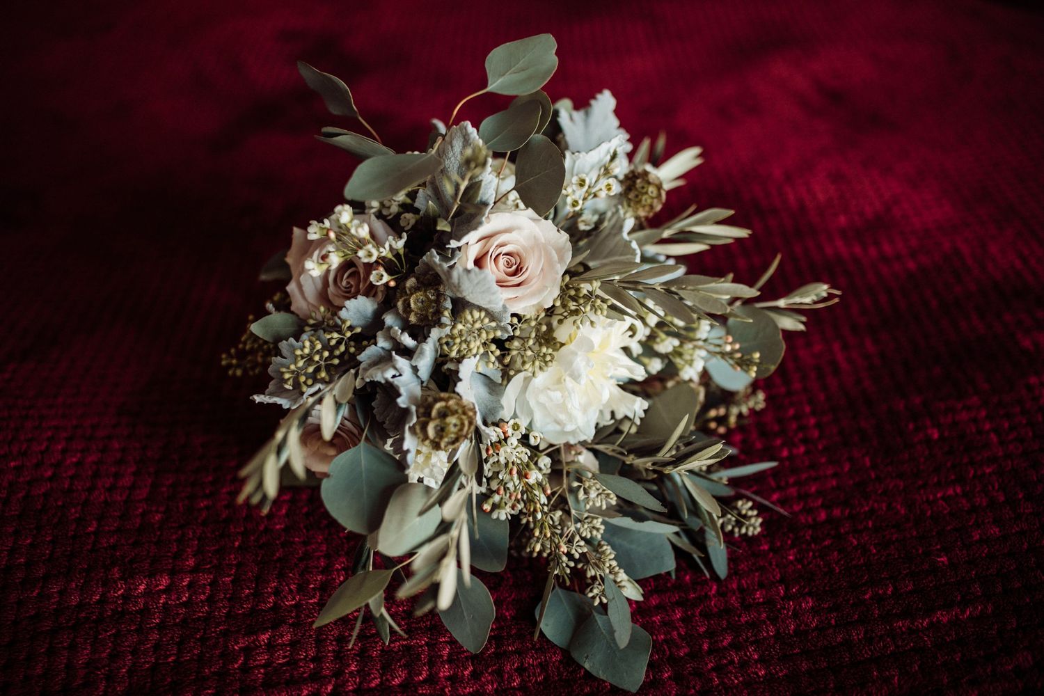 Elegant bridal bouquet with pink roses, white flowers, and eucalyptus on red velvet background.