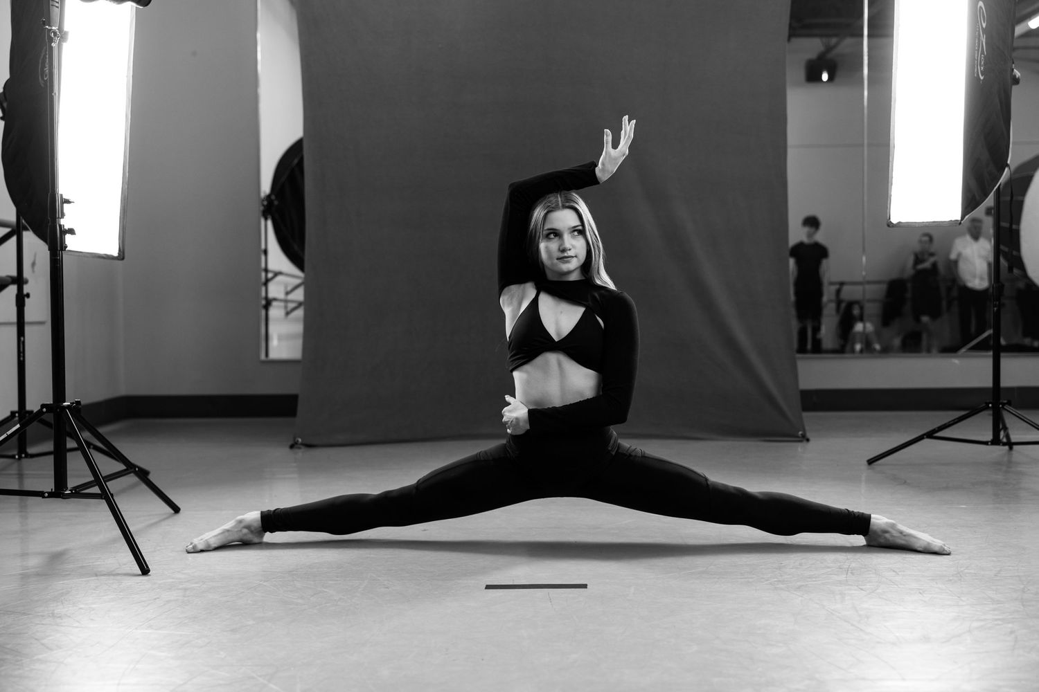 Black and white photo of dancer performing splits in a dance studio with professional lighting setup.