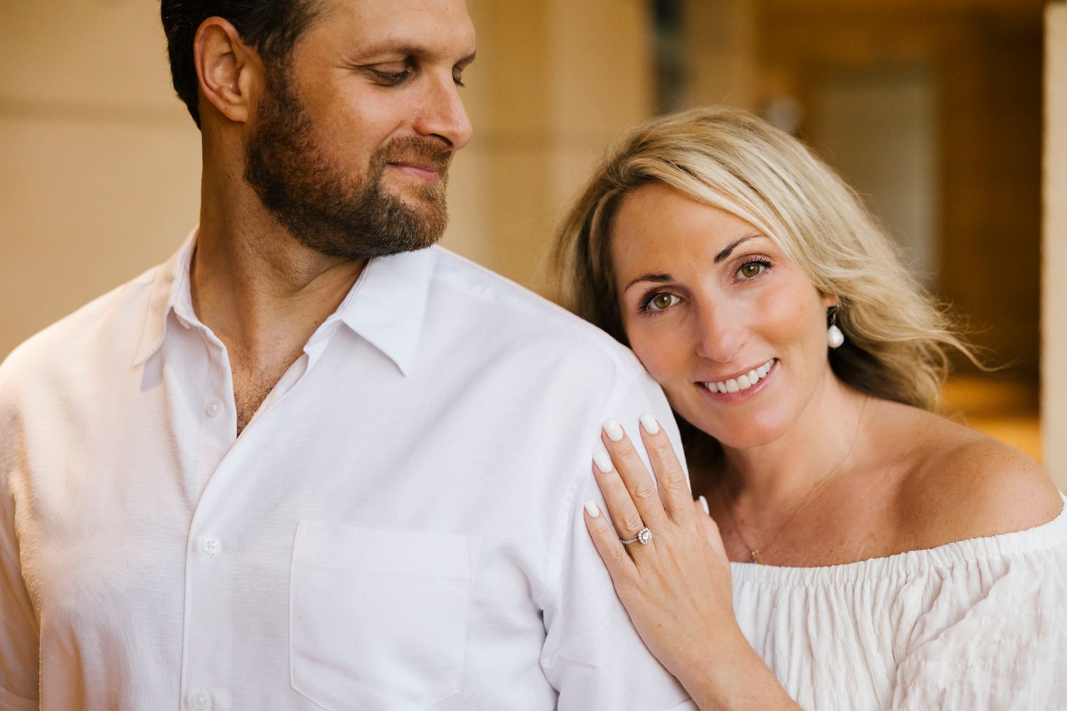 Couple in white outfits share intimate moment during engagement photoshoot.