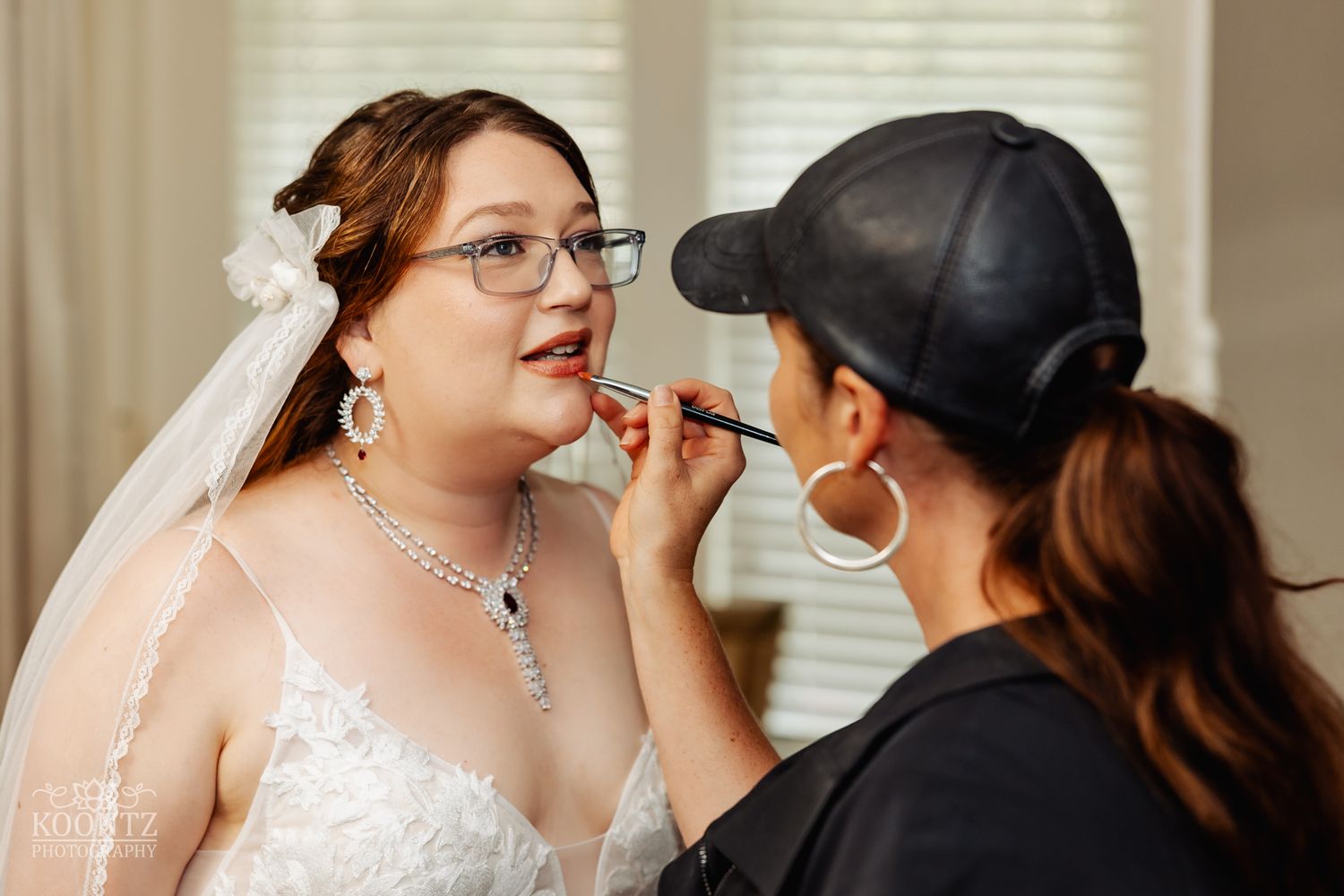 A makeup artist applies lipstick during bridal preparations in a sunlit room.