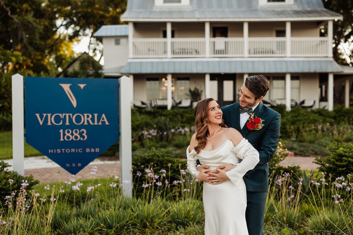 Bride and groom embracing and laughing in front of Victoria 1883 Historic Bar venue sign.