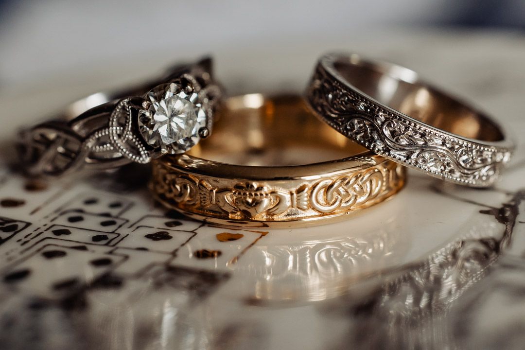 Three ornate wedding rings displayed together, featuring gold claddagh and diamond engagement ring designs.