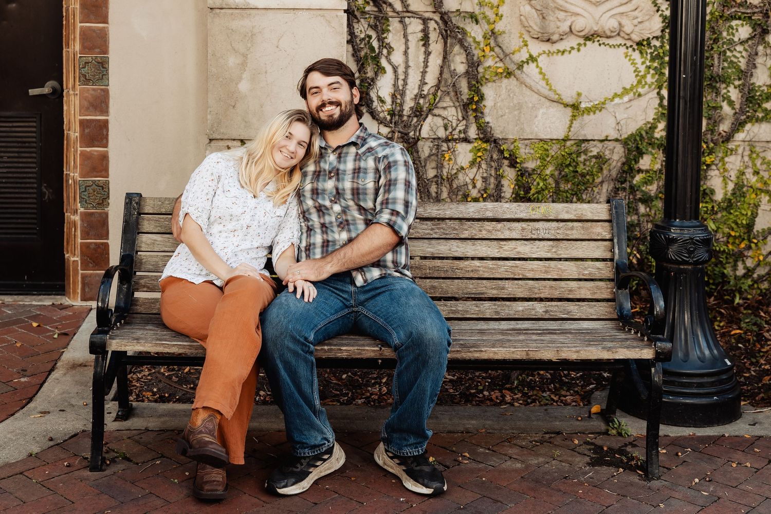 Happy couple sitting close together on a bench, woman in floral top and rust orange pants.