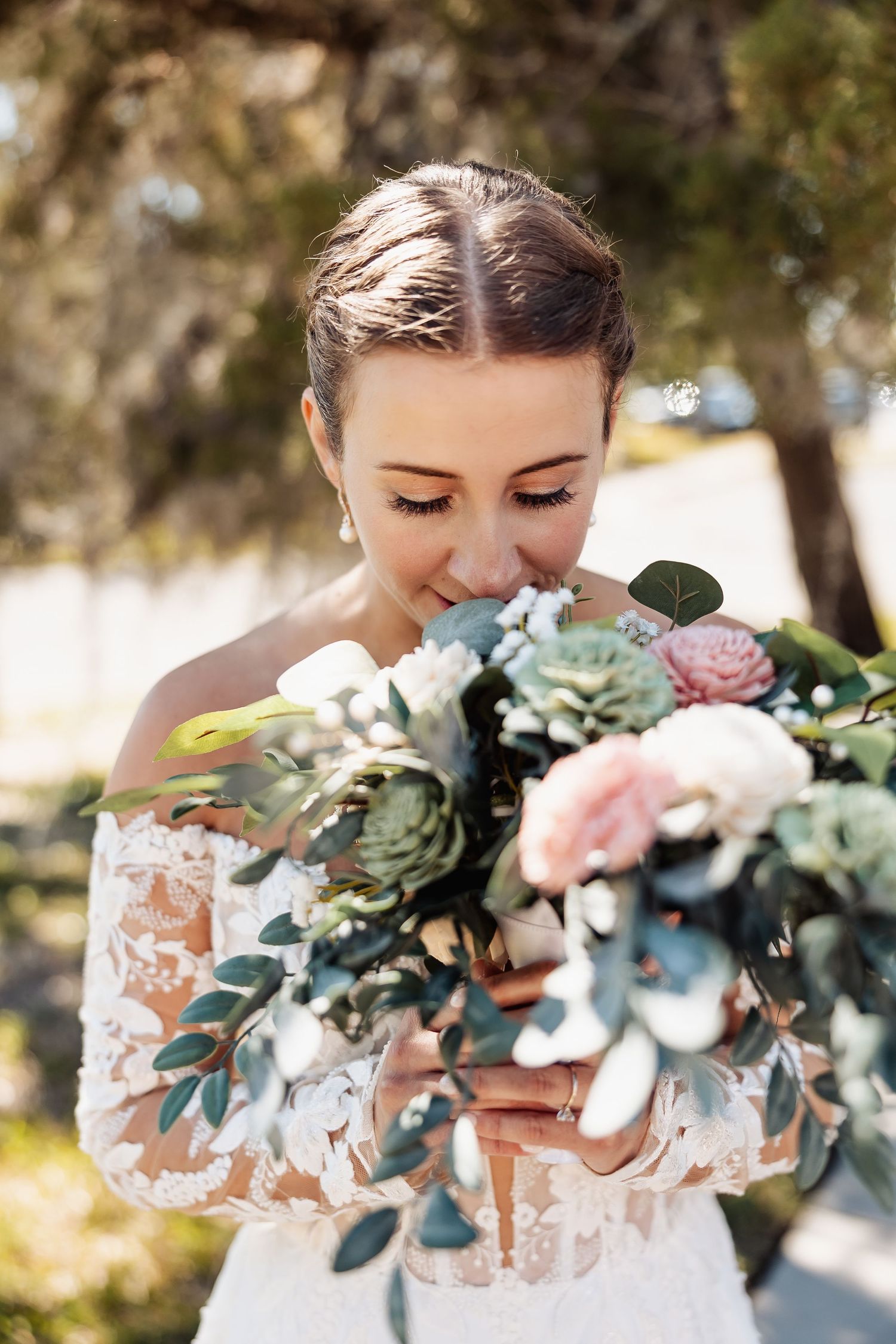 Bride in lace off-shoulder gown smelling a beautiful bouquet of pink and green flowers.