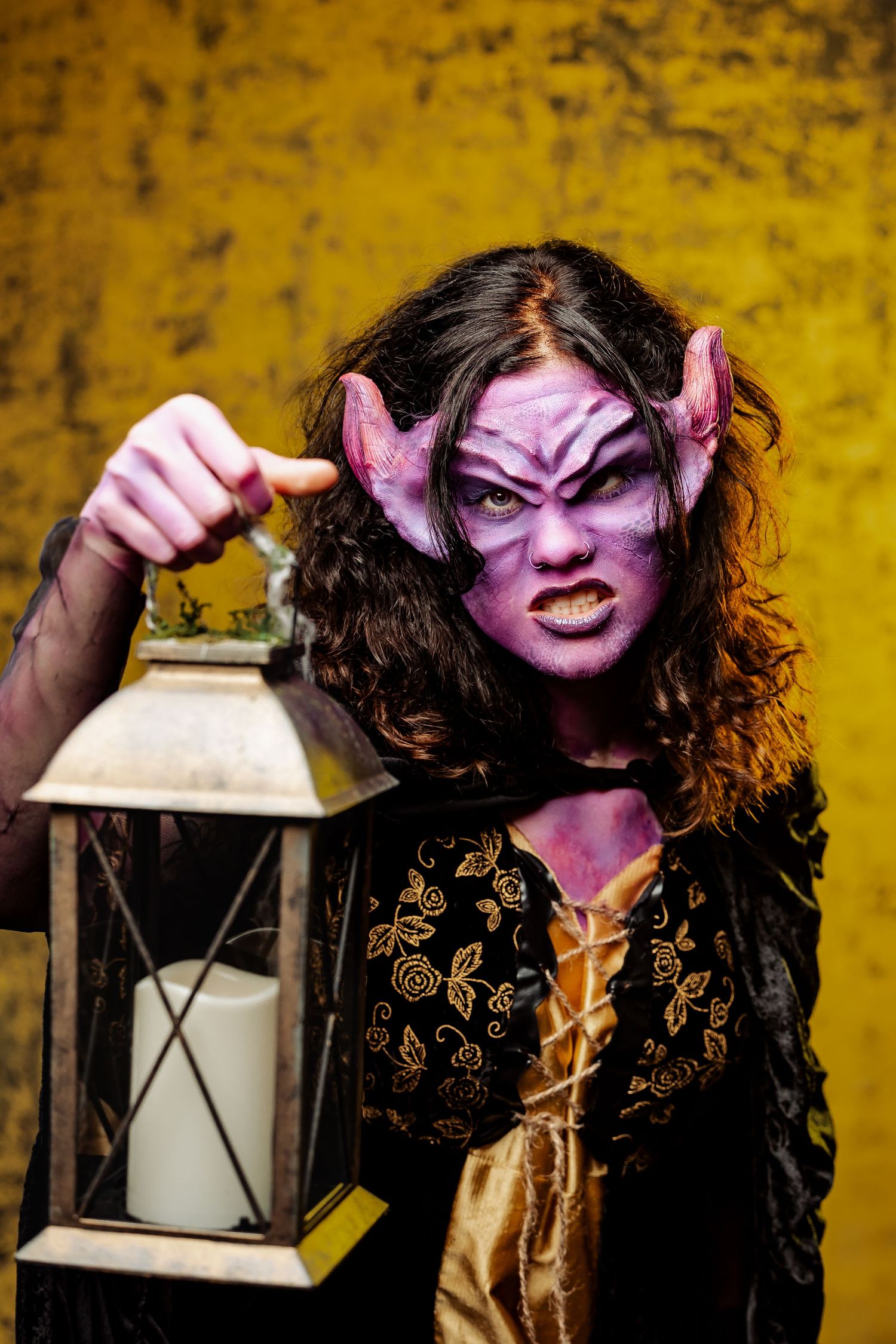 Fantasy creature in dark costume holding lantern against textured yellow wall.