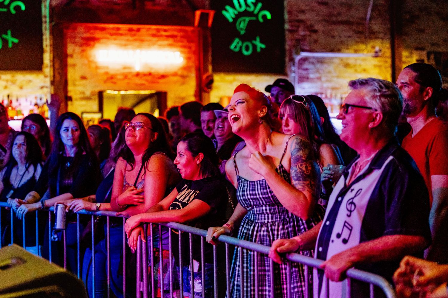 Excited concert crowd watches live music performance at the Music Box venue behind metal barriers.