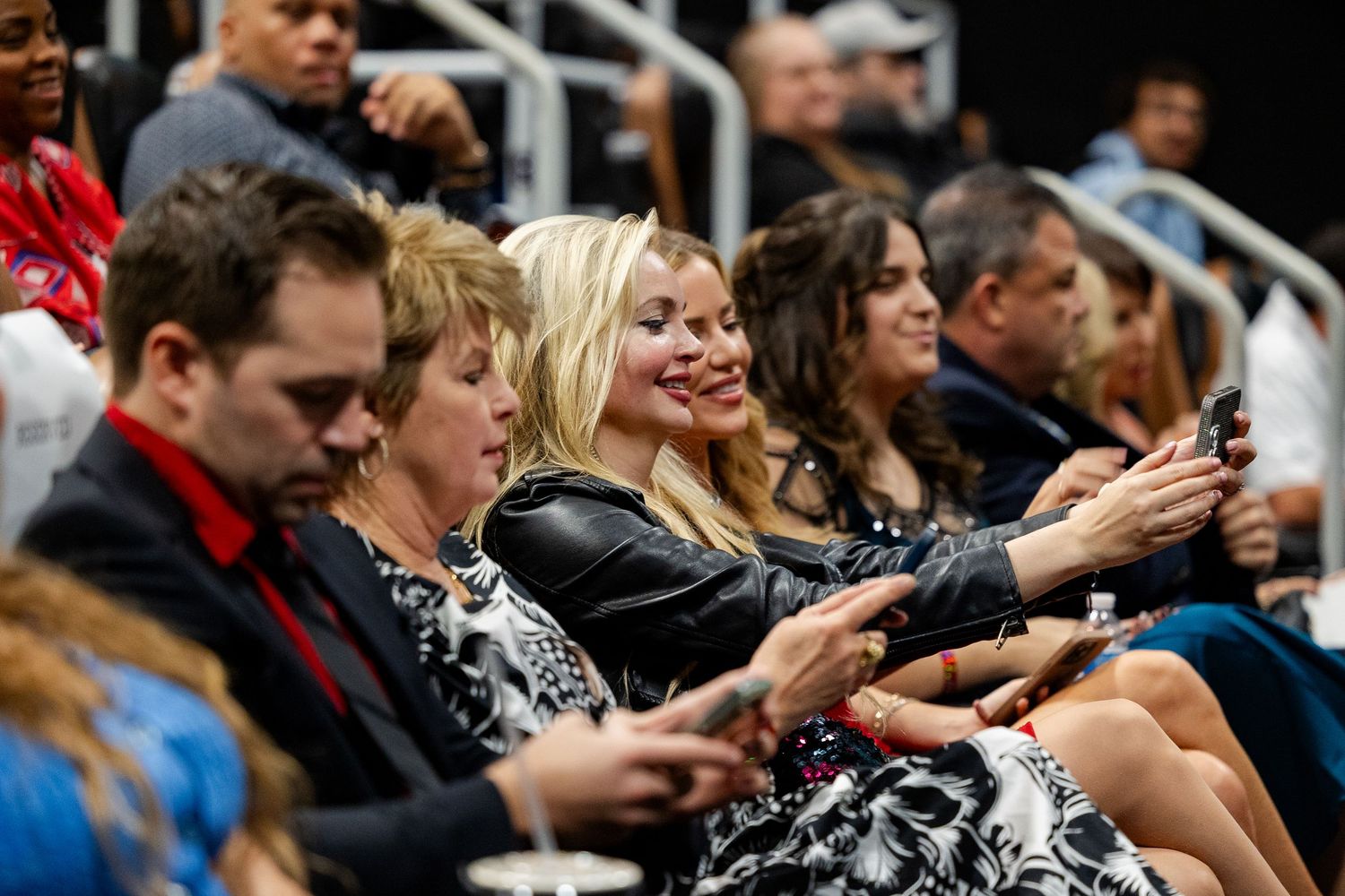 Audience members smile and use phones while seated at an indoor movie premiere screening.