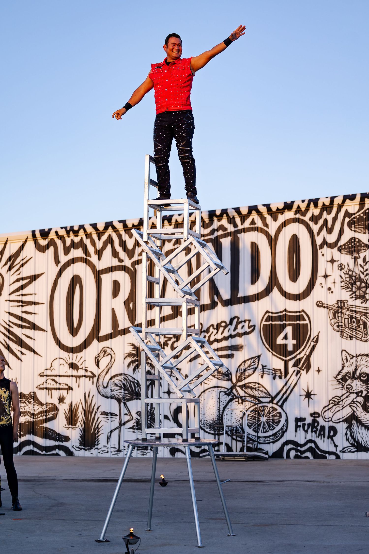 Circus performer standing triumphantly atop a tall ladder in front of an Orlando Florida mural.