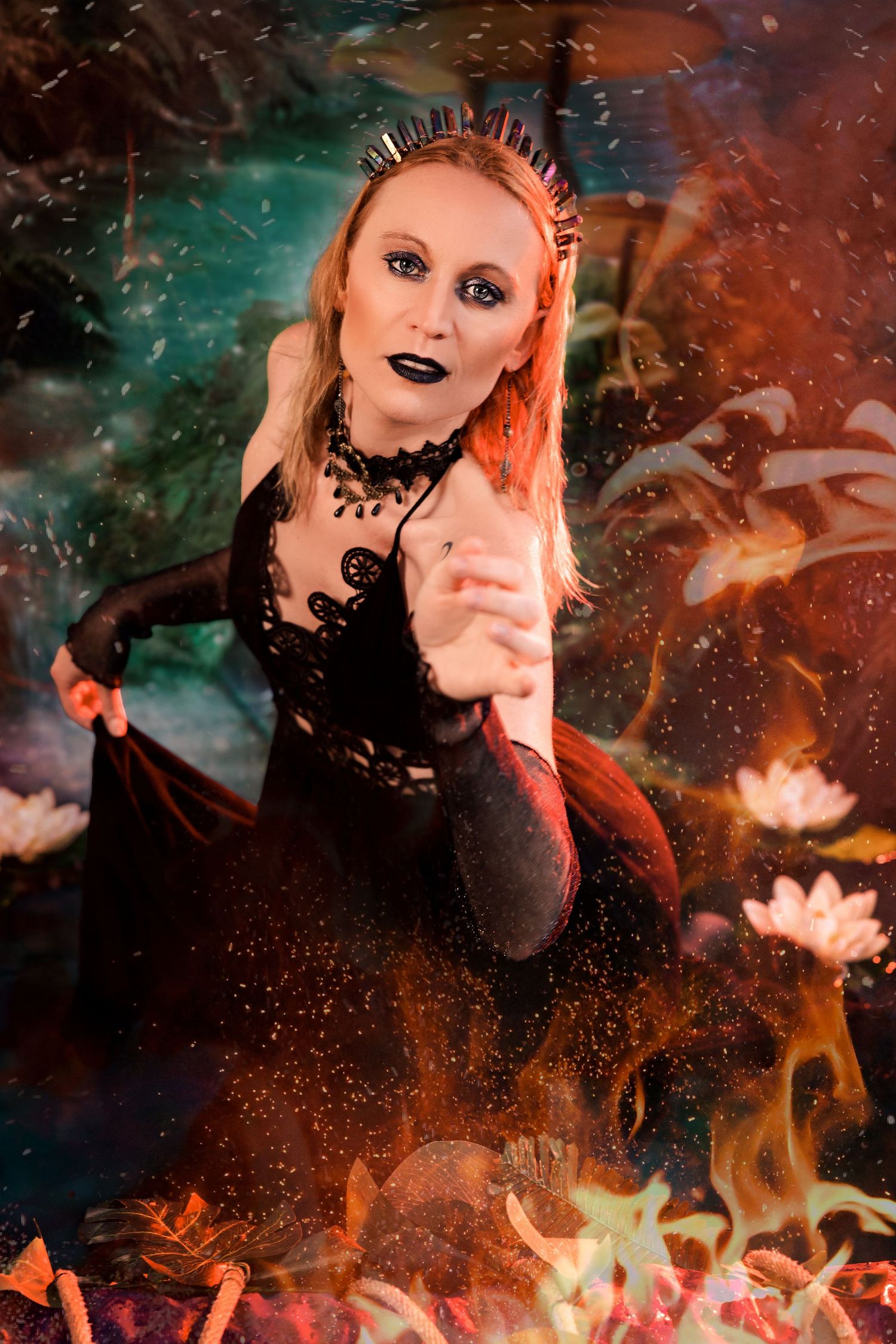 Blonde woman in dark queen costume with spiked crown poses amid fire and water lilies in fantasy scene.