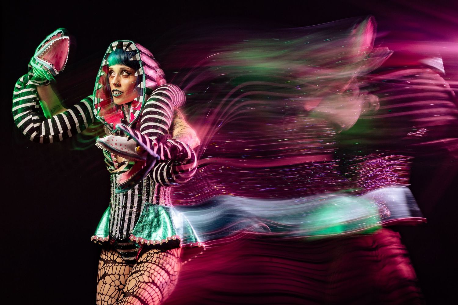 Colorful circus performer in striped costume surrounded by dynamic pink light trails in dark setting.