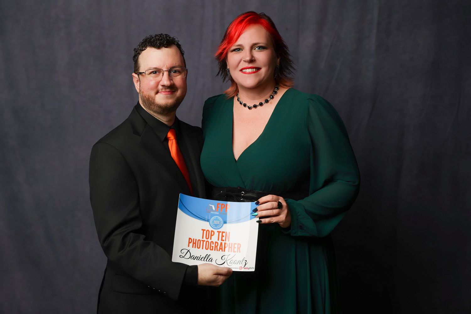 Man and woman in formal attire holding a Top Ten Photographer award certificate at a professional photography event.