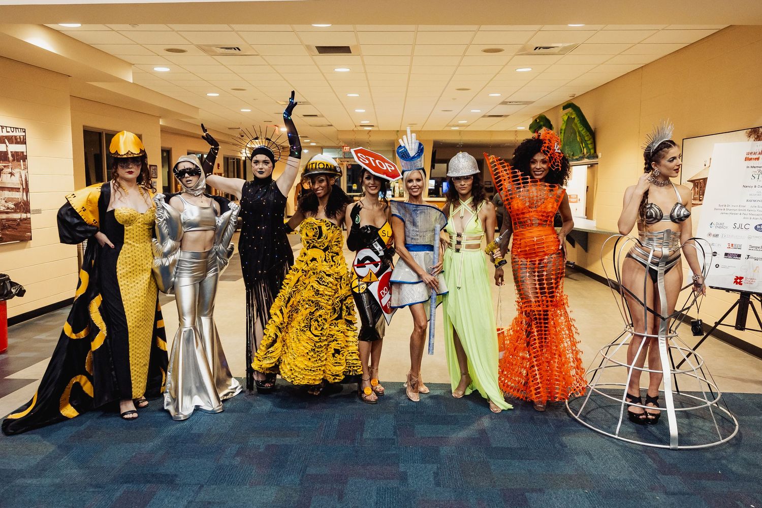 Group of models pose backstage in elaborate avant-garde construction-themed fashion show costumes.