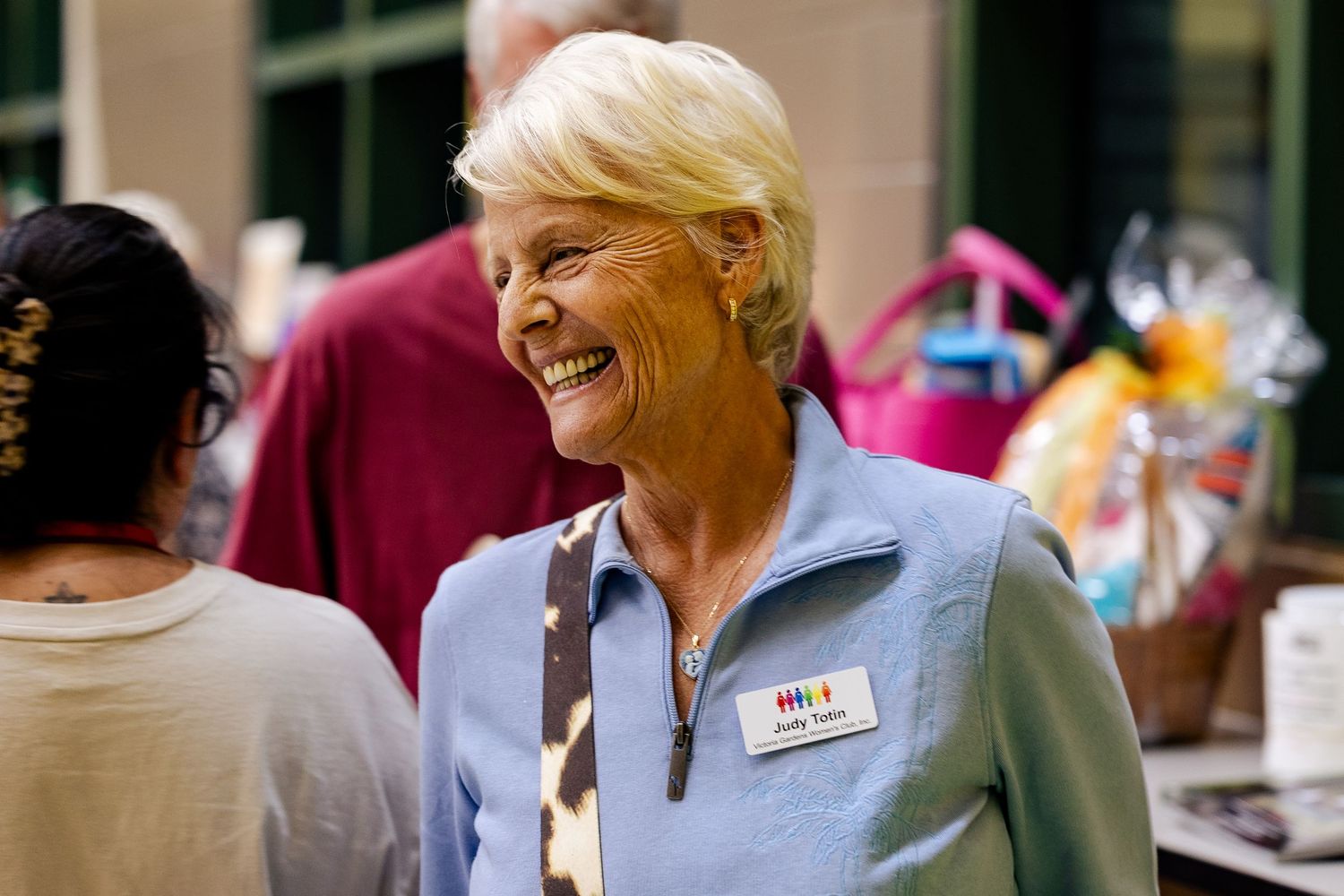 A smiling senior woman with a name tag enjoys a cheerful moment at an outdoor community event.