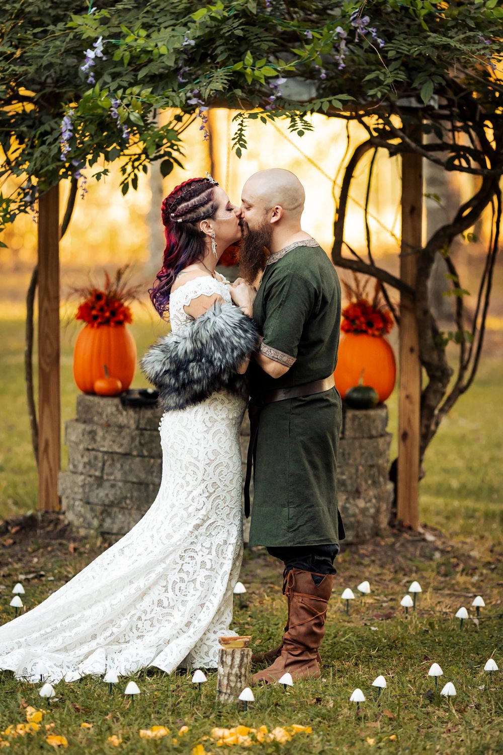 Viking wedding couple shares first kiss under vine-covered arch with pumpkins and fall foliage backdrop.