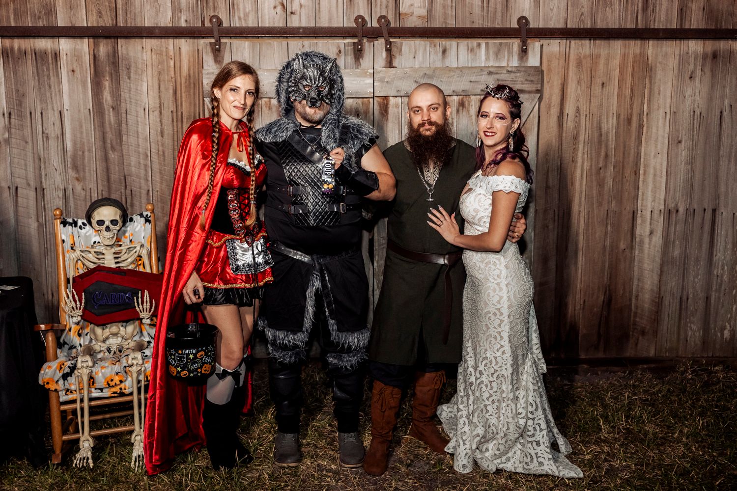 A Halloween-themed wedding group photo featuring costumes and spooky decorations against a wooden backdrop.
