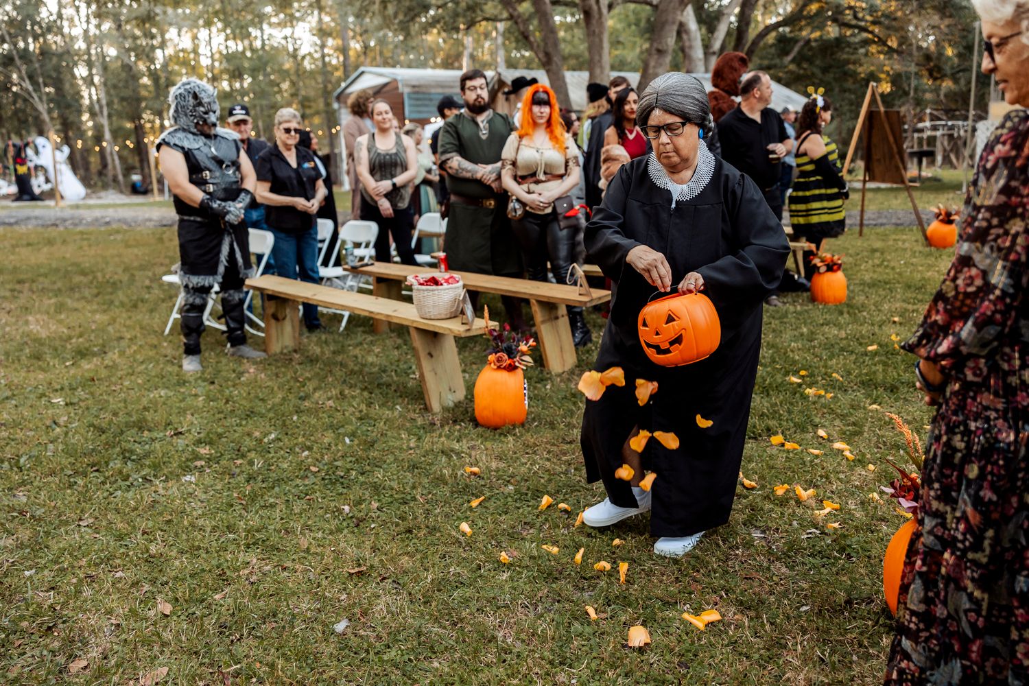 A Halloween-themed wedding celebration with guests gathered around wooden benches and decorated pumpkins.