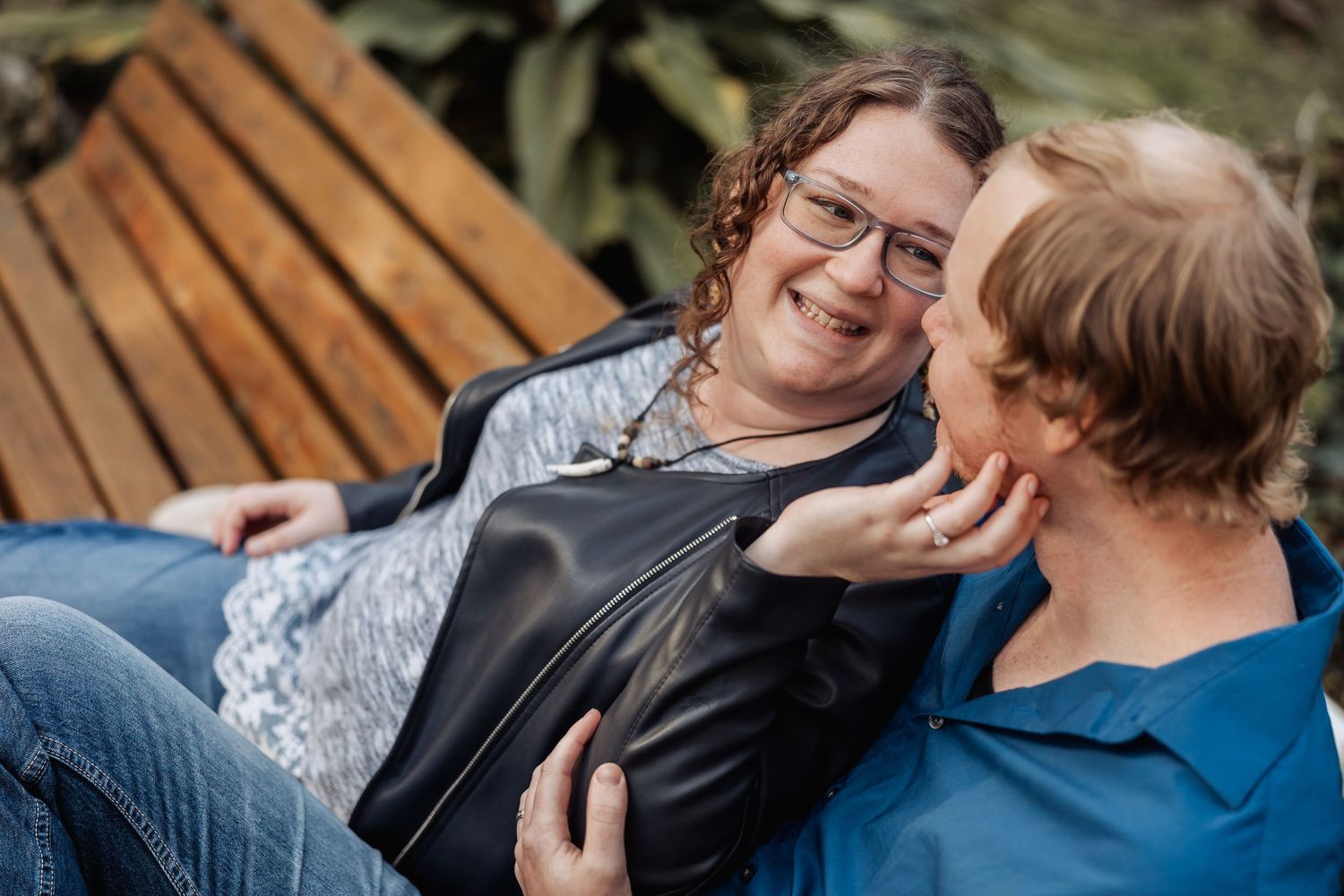 Two women laughing and smiling together on a wooden bench in a garden setting.