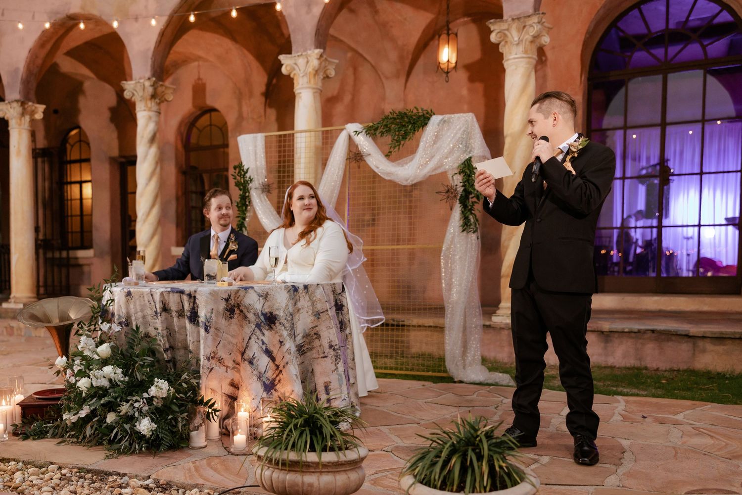 Wedding guest giving toast while bride and groom sit at sweetheart table.