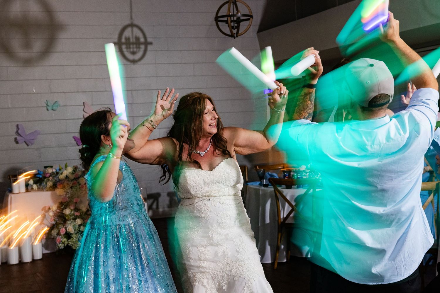 Bride dancing joyfully with guests holding colorful LED foam sticks at a lively wedding reception.