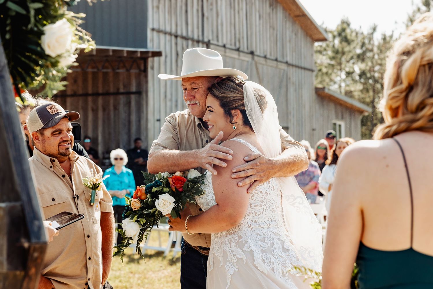 A joyful embrace at a rustic barn wedding ceremony with guests looking on in the background.