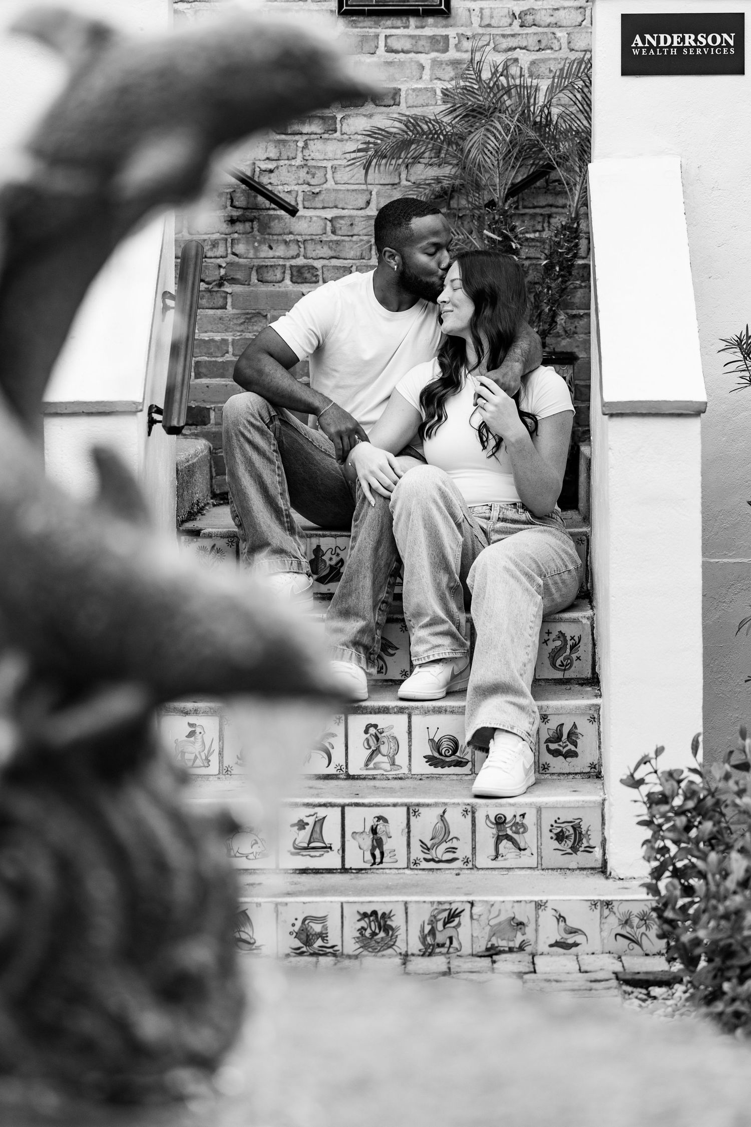A black and white photo of a couple sharing an intimate moment on tiled steps.