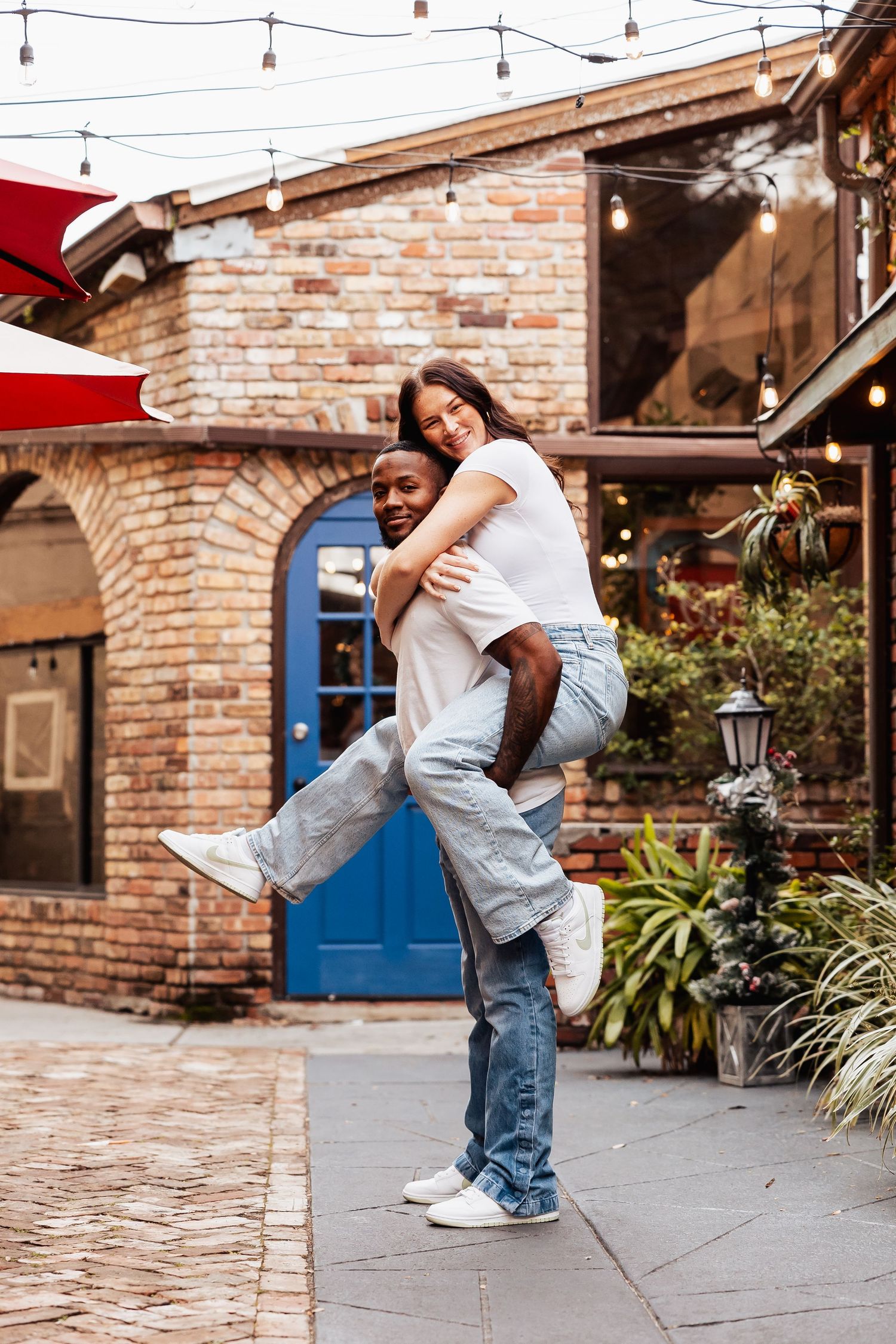 Playful couple poses in courtyard with string lights and blue door backdrop.