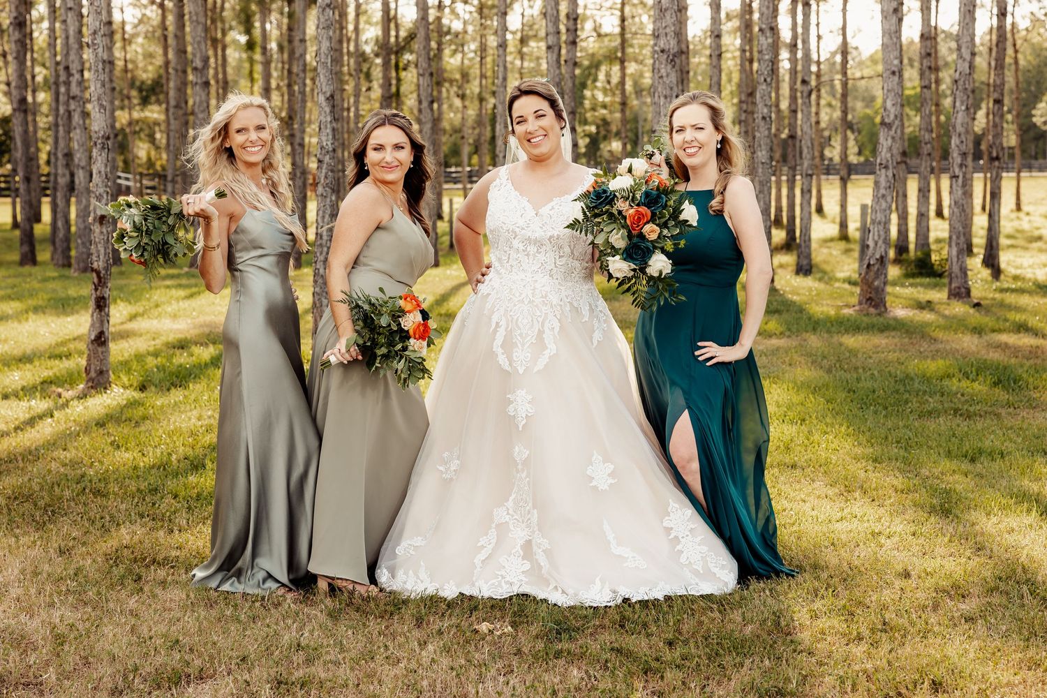 Bridal party in mixed jewel-toned dresses poses among tall pine trees.