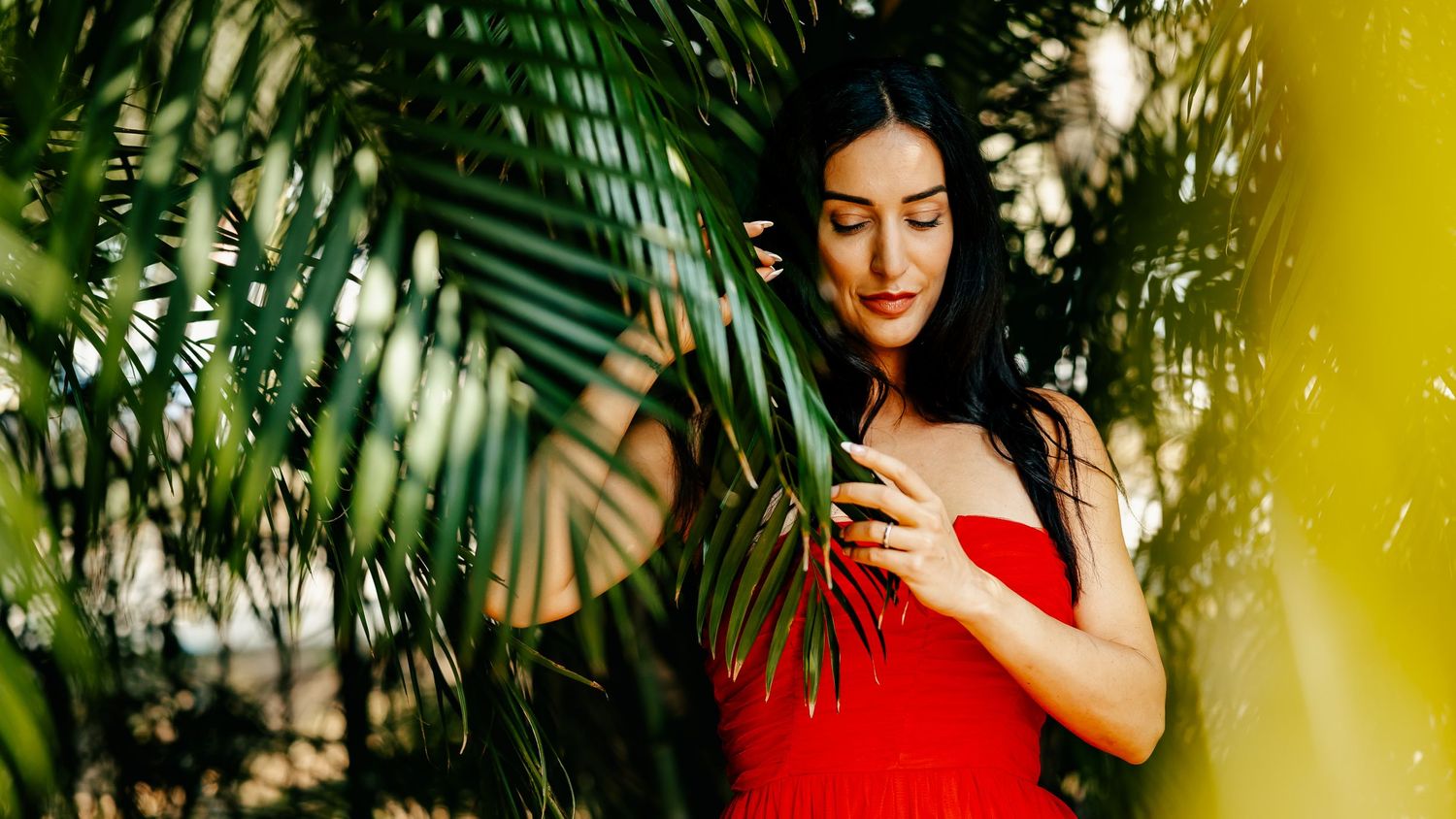 Artistic fashion photo amid tropical foliage with dramatic lighting and a red dress.