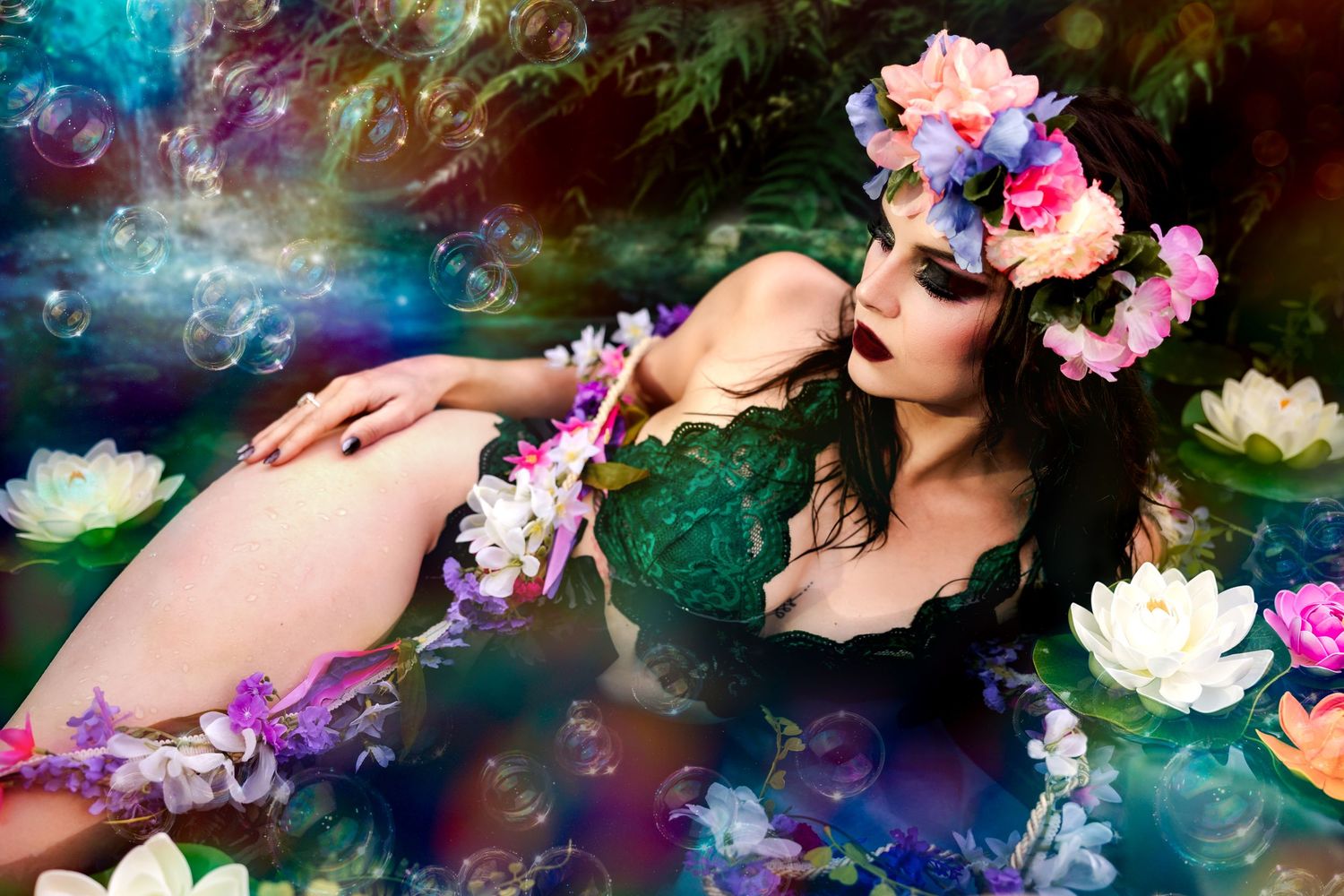Woman in green lace top with colorful flower crown floating among water lilies and soap bubbles.
