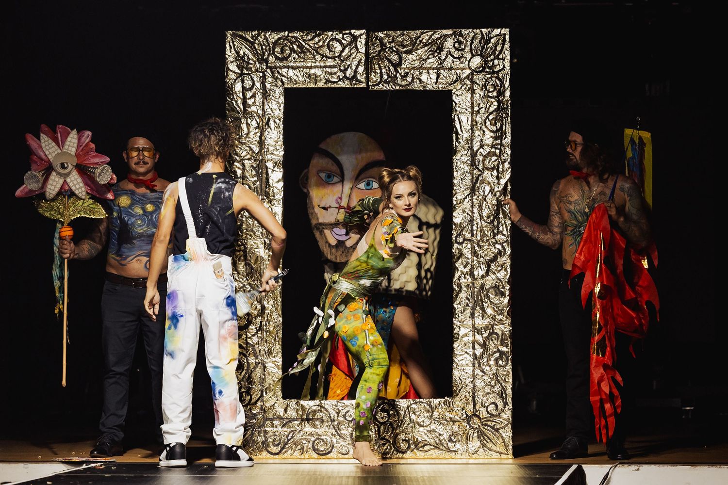 Models posing inside an ornate decorative frame prop on a fashion stage.