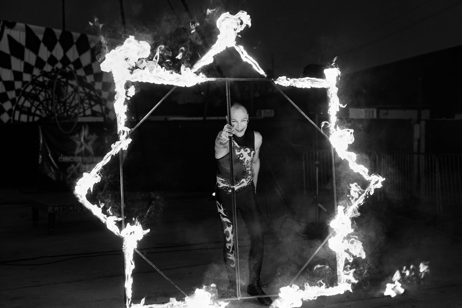 Black and white photo of circus performer standing inside a burning star-shaped fire frame.