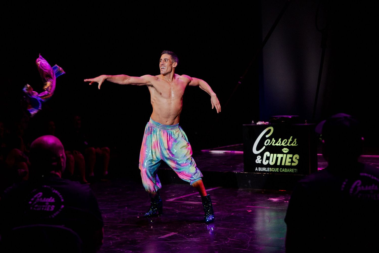 Shirtless male burlesque dancer in colorful pants performing on stage at Corsets and Cuties cabaret.