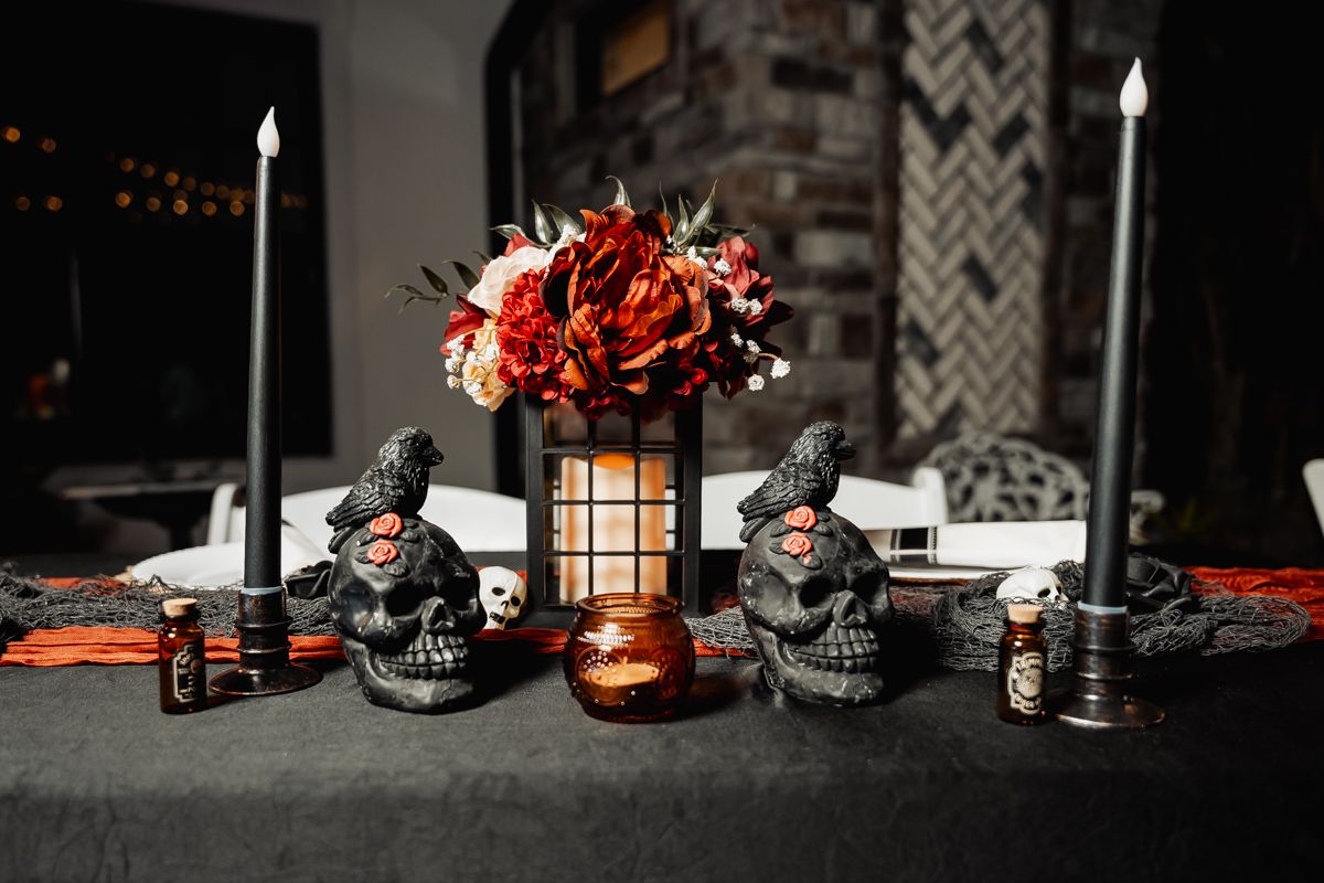 Halloween themed table decor with black skull decorations and candles in a dark moody setting.