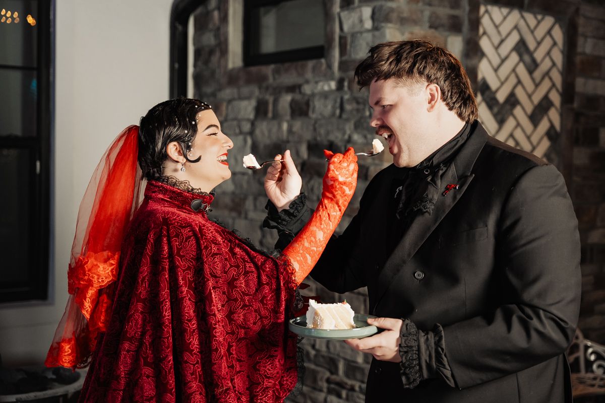 A couple in a romantic moment with one wearing a vibrant red dress against a dark background.